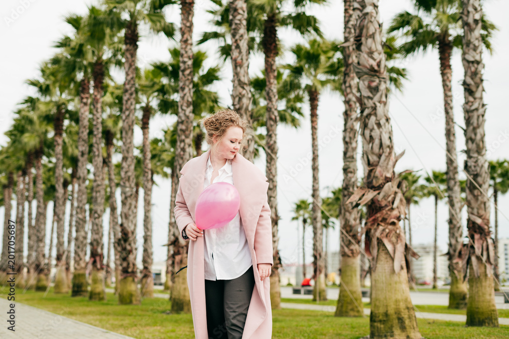 Fototapeta premium stylish attractive young woman in a coat holds a pink balloon and walks in the park