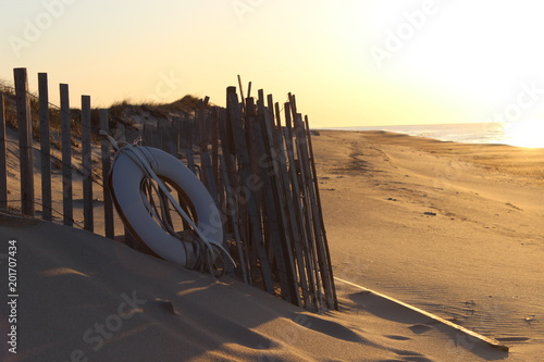 White life preserver buoy and rope on fence in the sandy dunes of coastal beach at sunset 