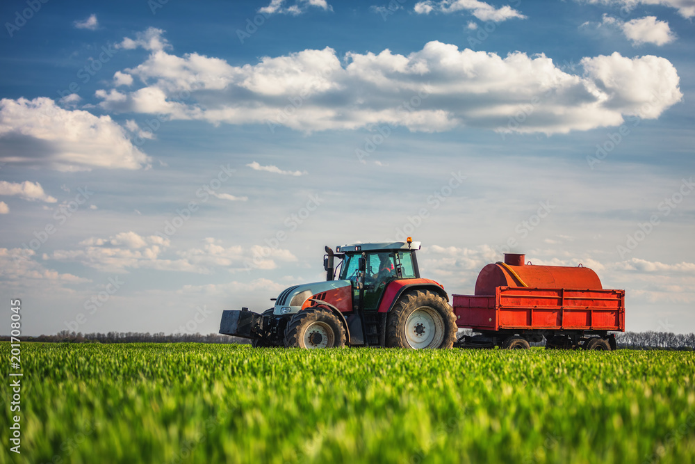 Naklejka premium Farming tractor plowing and spraying on field