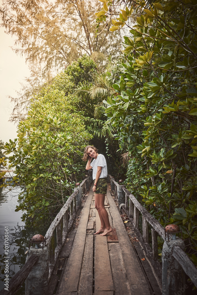 Traveling girl on the wooden bridge. Pretty young woman in the jungle. Summer lifestyle and adventure photo Traveling girl on the wooden bridge. Pretty young woman in the jungle. Summer lifestyle and adventure photo
