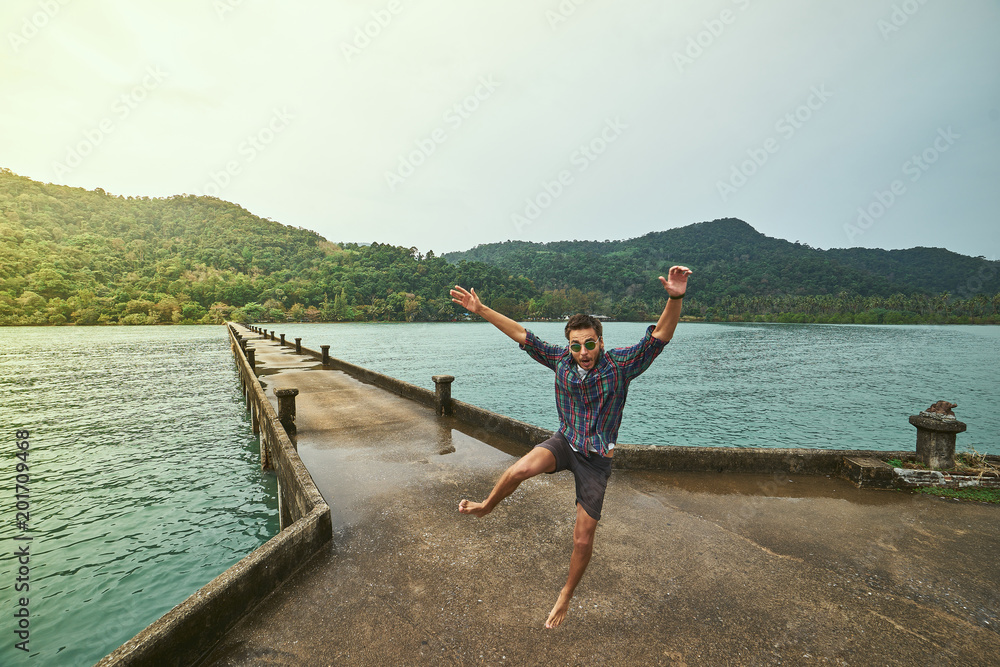 Traveling boy on the pier. Pretty young man jumping on the bridge. Summer lifestyle and adventure photo