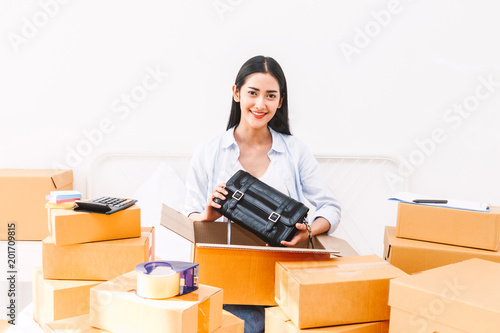 Young woman freelancer working sme business online shopping and packing woman bag with cardboard box on bed at home - Business online shipping and delivery concept