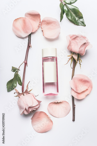 Pink cosmetic bottle with facial roses water or toner with essential oil , flowers and petals on white desk background, top view, branding mock up and copy space. Roses essence