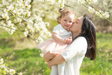 Mum embraces the child and kisses, in the blossoming spring gardens