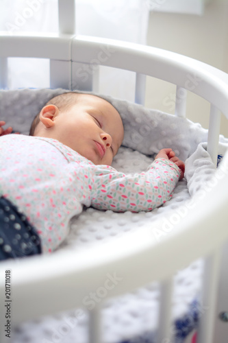 Newborn baby at home. New born child in wooden co-sleeper crib. Infant sleeping in bedside bassinet. Little girl taking a nap.