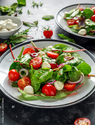 Fresh Cherry Tomato, Mozzarella salad with green lettuce mix and red onion. served on plate. healthy food.