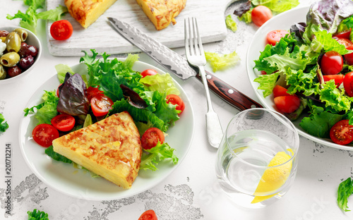 Spanish tortilla, omelette with potato, onion, vegetables, tomatoes, olives and herbs in a white plate. breakfast, healthy food.