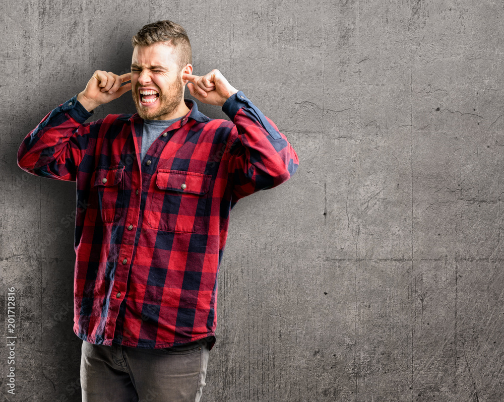 Young handsome man covering ears ignoring annoying loud noise, plugs ears to avoid hearing sound. Noisy music is a problem. Young handsome man covering ears ignoring annoying loud noise, plugs ears to avoid hearing sound. Noisy music is a problem.