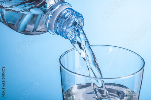 Pouring water from bottle into glass on blue background.