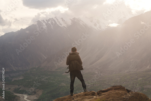 Traveller with backpack standing on mountain peak, enjoying beautiful sunset and valley view. Travel lifestyle and achievement success concept