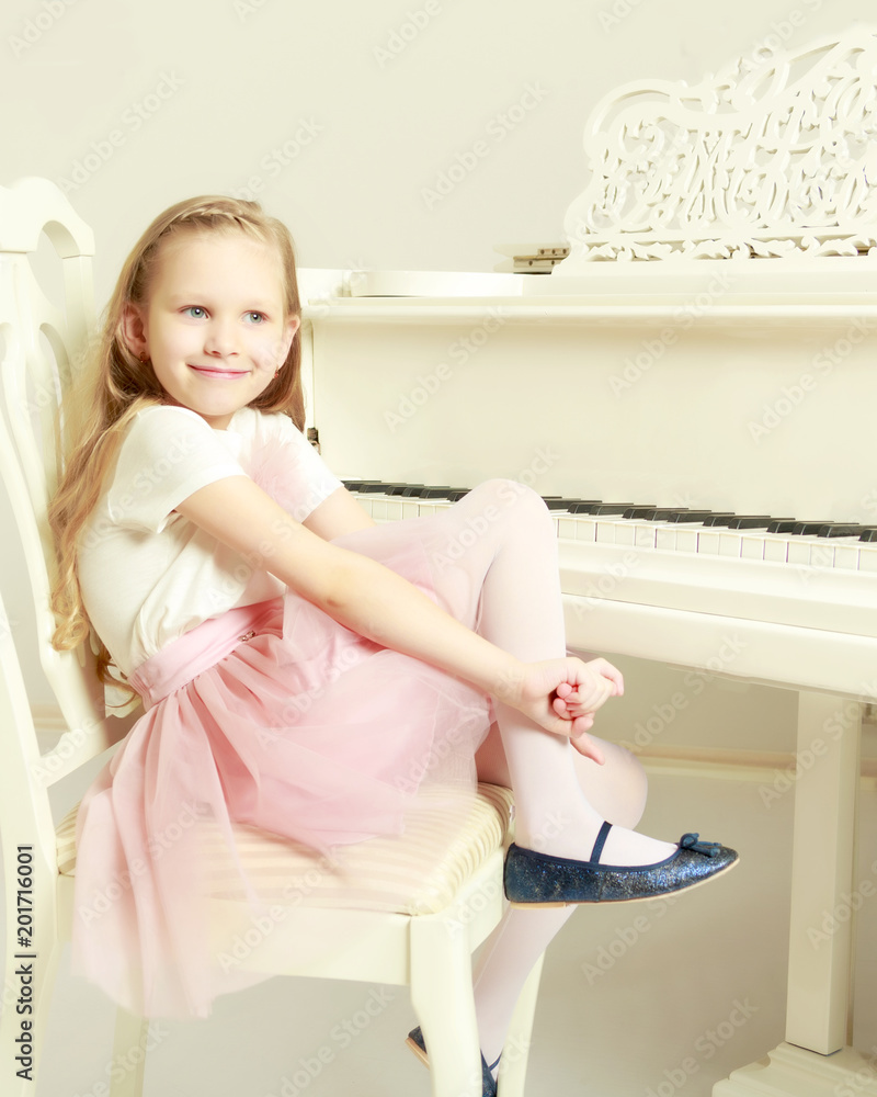 A little girl is sitting at the white piano. A little girl is sitting at the white piano.