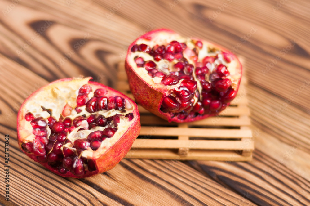 One half of red fresh ripe pomegranate with seeds on pallet beside one piece of pomegranate on old brown weathered wooden planks One half of red fresh ripe pomegranate with seeds on pallet beside one piece of pomegranate on old brown weathered wooden planks