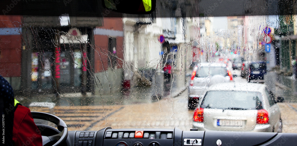 Obraz premium raindrops on the drivers bus window. clolful view on street traffic. urban backgruond.