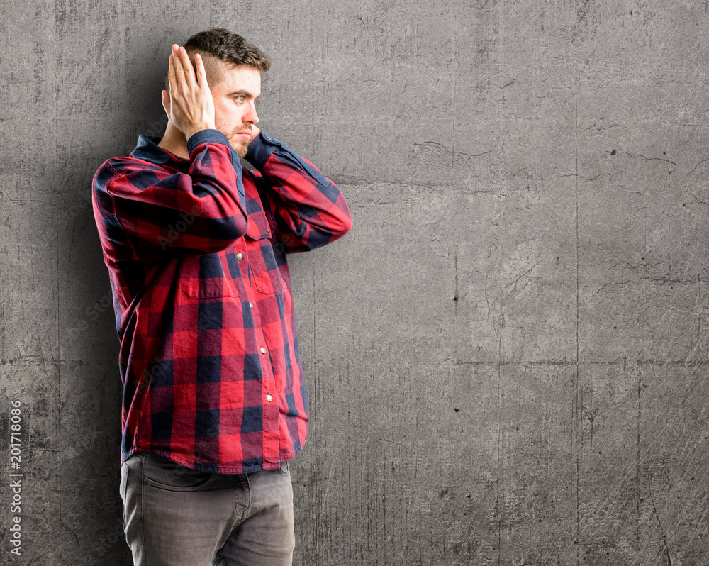 Young handsome man covering ears ignoring annoying loud noise, plugs ears to avoid hearing sound. Noisy music is a problem. Young handsome man covering ears ignoring annoying loud noise, plugs ears to avoid hearing sound. Noisy music is a problem.