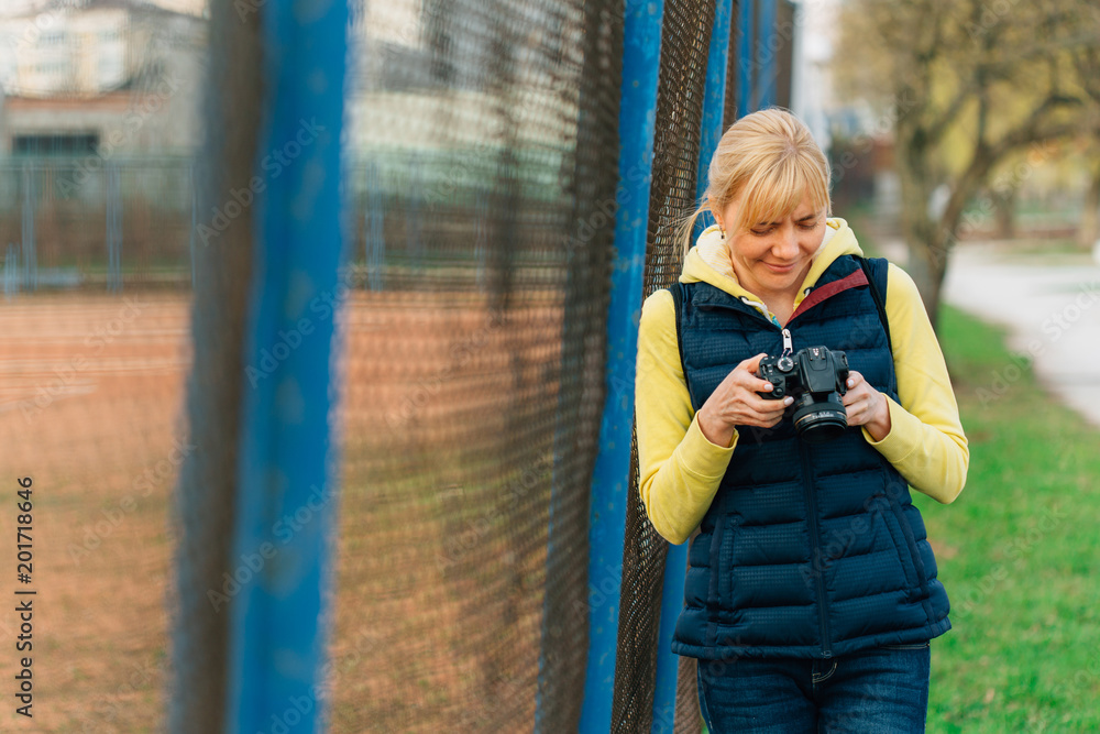 Obraz premium Girl with professional camera in hands. Close up of female photographer in park. Pretty smiling woman looking at the screen of camera