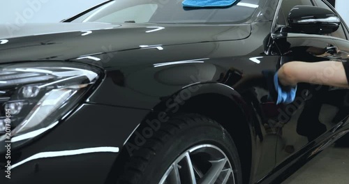 A professional worker holds a cloth in blue, wipes a black car, car repair shop, car washing.