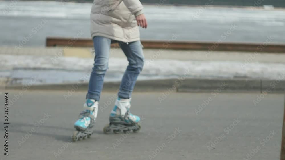 Young beautiful woman in a red hat, wearing sporty warm clothes and rollers, riding on the road on the coast Young beautiful woman in a red hat, wearing sporty warm clothes and rollers, riding on the road on the coast