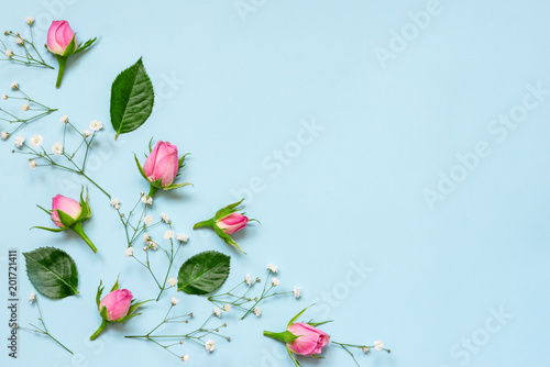 Obraz na płótnie Top view of pink roses and green leaves over blue background. Abstract floral background. Copy space. w salonie