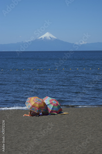 People sitting under colourful sun umbrellas on the shore of Lake Llanquihue at Frutillar in the Lake District of southern Chile.