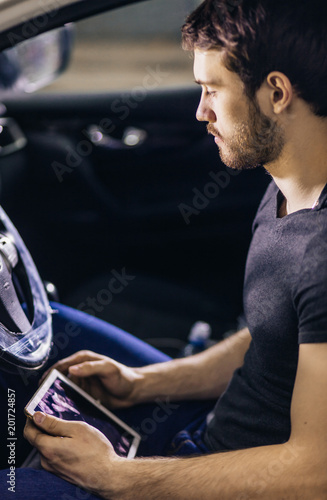 Mechanic Sitting In Car Looking At Digital Tablet in repair garage © alfa27