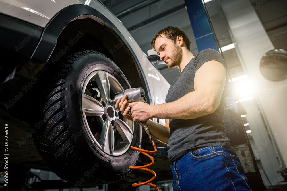 Mechanic changing tire in workshop vehicle using electric drill Mechanic changing tire in workshop vehicle using electric drill