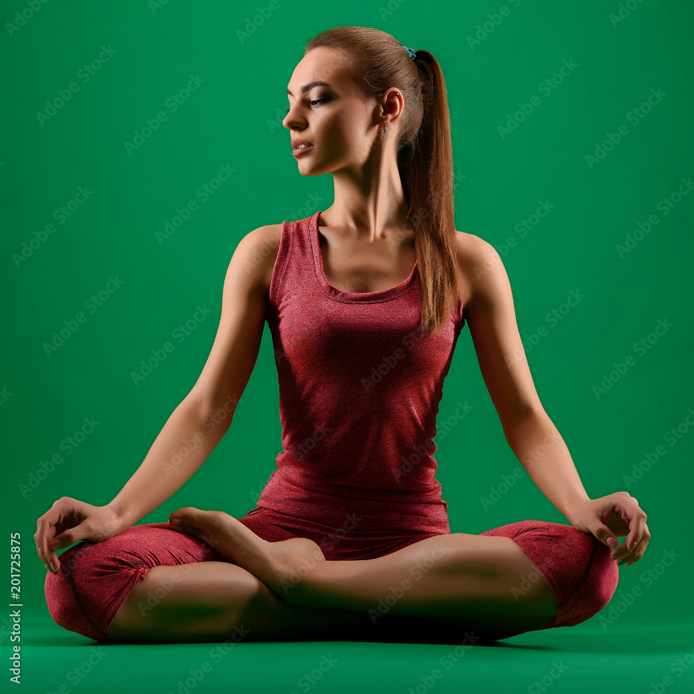 Obraz premium Slim woman's doing yoga in lotus pose, Padmasana, in red sport outfit isolated on green background