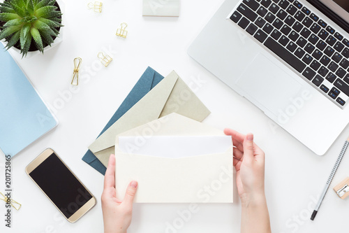 Fotografie Top view of woman hands opening envelope on white office table desk, flat lay