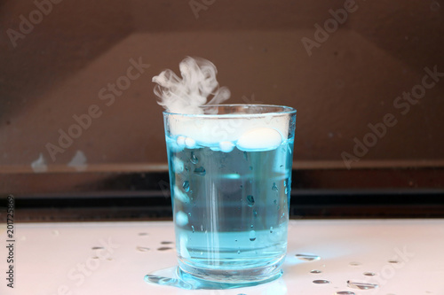 Tableau sur toile Dry ice in a glass of blue water and engender white smoke on white floor with black background