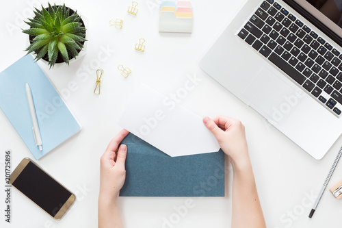 Top view of woman hands opening envelope on white office table desk, flat lay. View from above of different chancellery stuff, layout