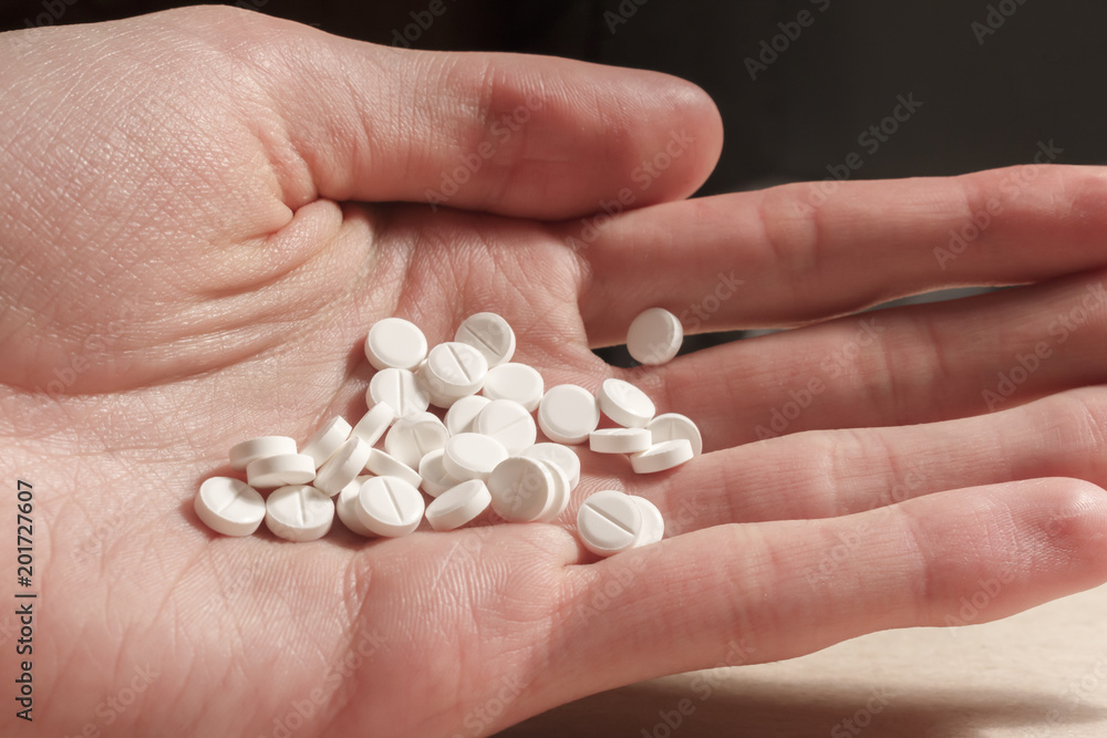 pile of white pills on the male hand. pile of white pills on the male hand.