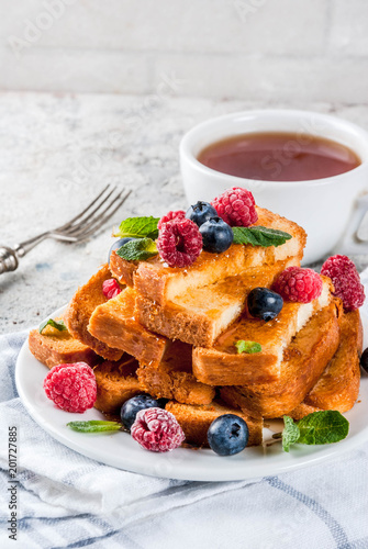Healthy summer breakfast, baked french toasted bread sticks with fresh berry and honey, morning light grey stone background copy space