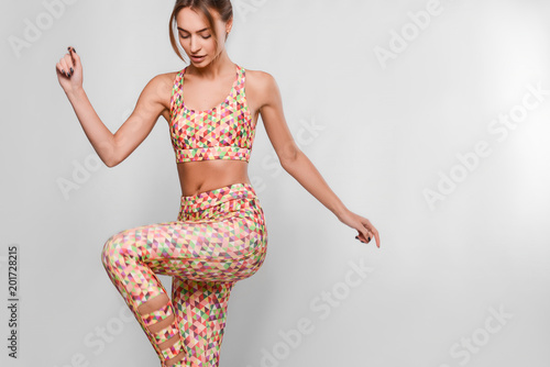 Slim young woman in sport outfit, tight colorful leggings and top with geometrical patterns in a motion, happy, joyful, jumping, isolated in studio