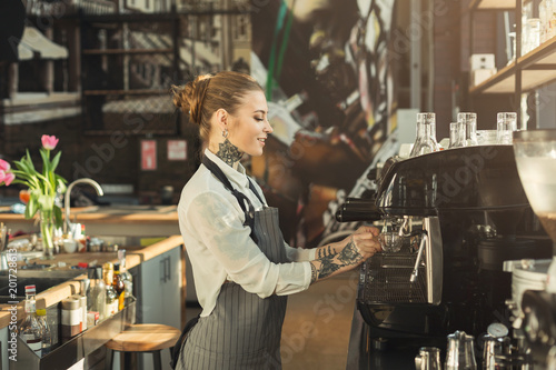 Tattooed barista making coffee in professional coffee machine photo