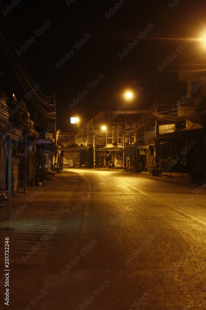 remote thai town main street at night time with rows of yellow shining street lights, Northern Thailand, Southeast Asia