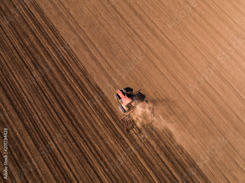 Aerial shot of a tractor cultivating field at spring