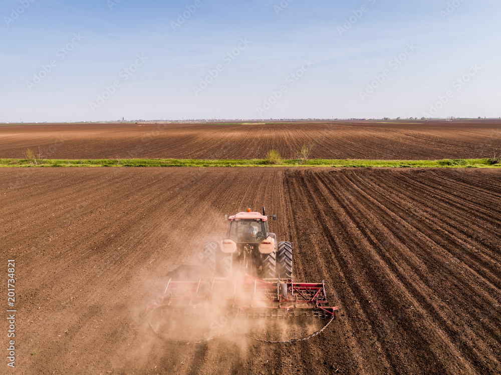 Obraz premium Aerial shot of a tractor cultivating field at spring