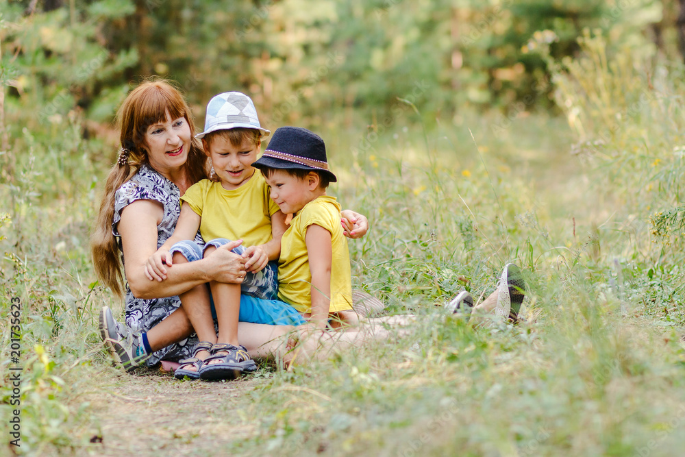 young happy grandmother with two little grandchildren sitting on a forest lawn and laughing in the summer young happy grandmother with two little grandchildren sitting on a forest lawn and laughing in the summer