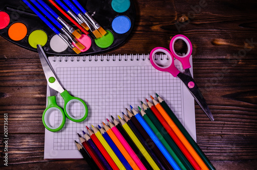 Set of different school stationeries. Notepad, scissors, pensils, paints, paintbrushes on wooden desk. Back to school. Top view