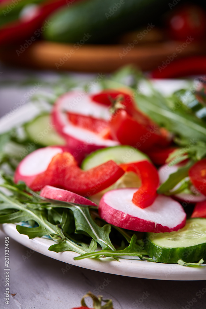 Wooden plate with vegetables for a vegetarian salad on white textured background, close-up, selective focus Wooden plate with vegetables for a vegetarian salad on white textured background, close-up, selective focus