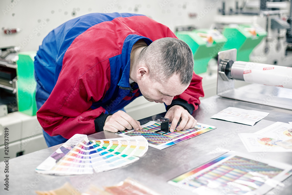 Operator in printing factory control colours with magnifying glass
