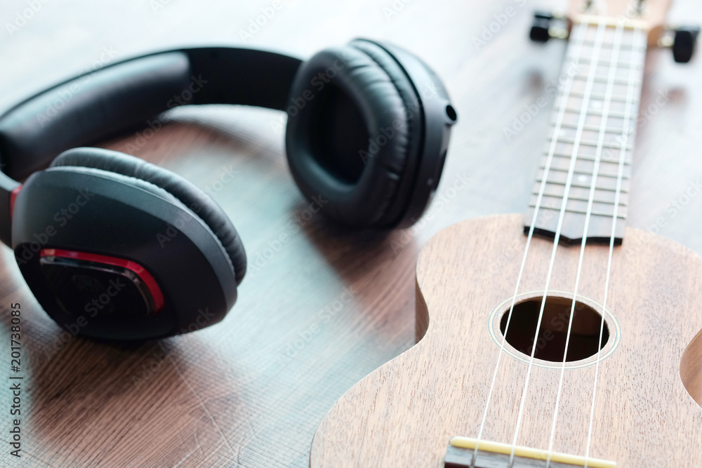 Headphones and acoustic guitar ukulele brown on wooden floor. Headphones and acoustic guitar ukulele brown on wooden floor.