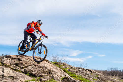 Fototapeta Naklejka Na Ścianę i Meble -  Cyclist in Red Jacket Riding Mountain Bike Down Rocky Hill. Extreme Sport and Adventure Concept.