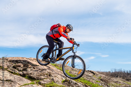 Fototapeta Naklejka Na Ścianę i Meble -  Cyclist in Red Jacket Riding Mountain Bike Down Rocky Hill. Extreme Sport and Adventure Concept.