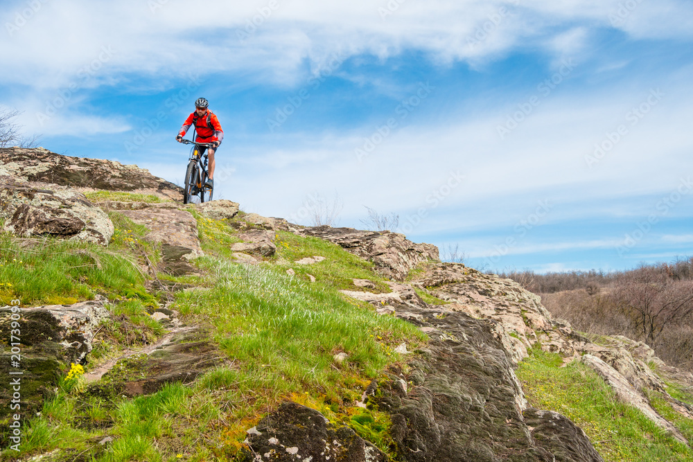 Cyclist in Red Jacket Riding Mountain Bike Down Rocky Hill. Extreme Sport and Adventure Concept.