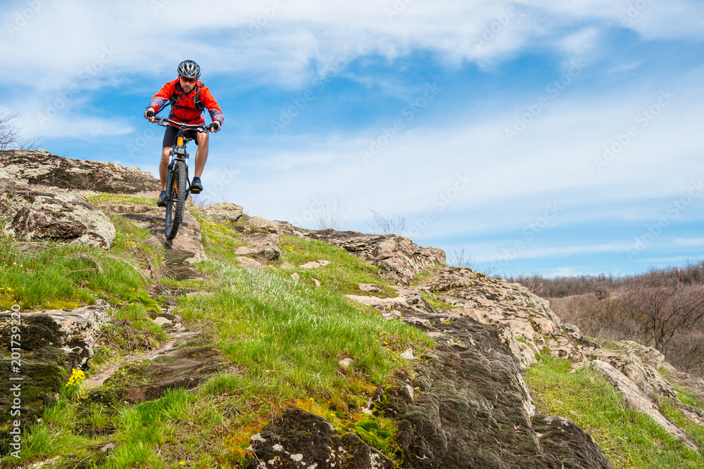 Cyclist in Red Jacket Riding Mountain Bike Down Rocky Hill. Extreme Sport and Adventure Concept.