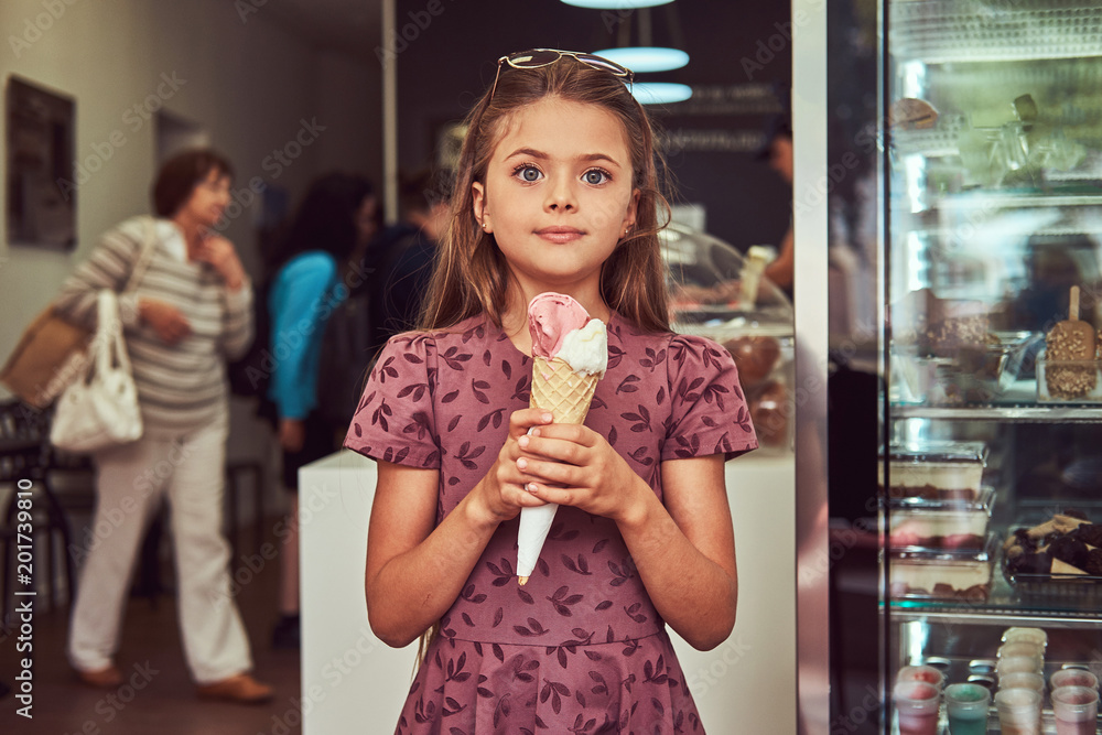 Beauty little girl in a fashionable dress eating strawberry, standing in an ice cream parlor. Beauty little girl in a fashionable dress eating strawberry, standing in an ice cream parlor.