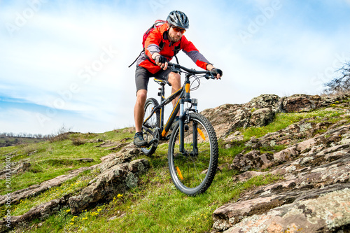 Cyclist in Red Jacket Riding Mountain Bike Down Rocky Hill. Extreme Sport and Adventure Concept.