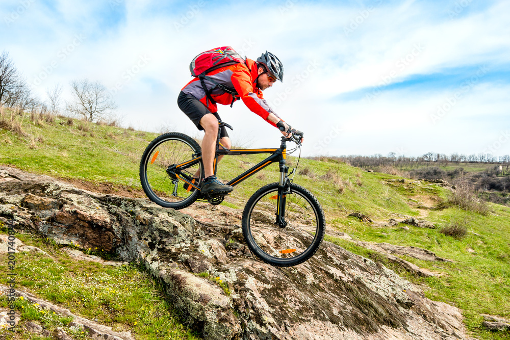 Cyclist in Red Jacket Riding Mountain Bike Down Rocky Hill. Extreme Sport and Adventure Concept. Cyclist in Red Jacket Riding Mountain Bike Down Rocky Hill. Extreme Sport and Adventure Concept.