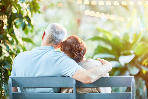 Fotografie Back view of affectionate senior spouses having rest on bench in natural environ