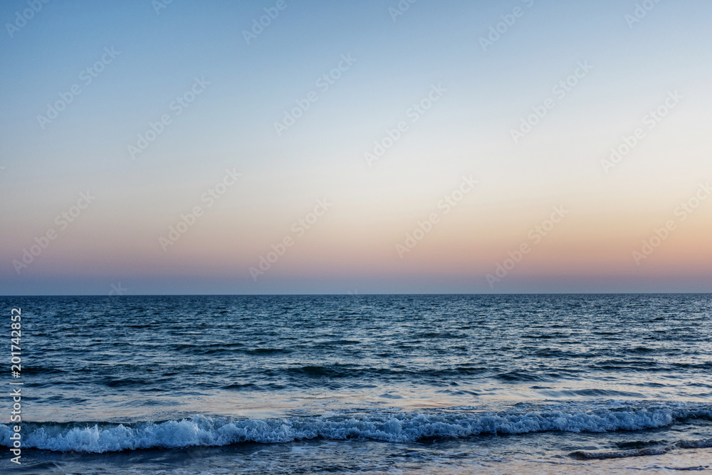 blue sea at sunset. the waves are to the shore. the sun over the horizon